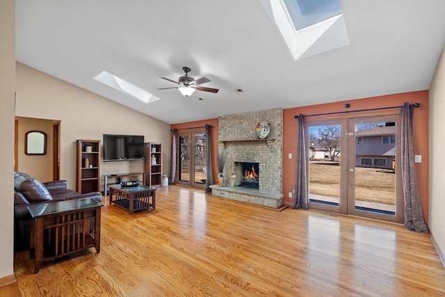 living area featuring vaulted ceiling with skylight, a fireplace, a ceiling fan, and wood finished floors