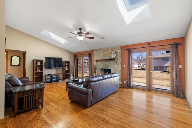 living area with ceiling fan, lofted ceiling with skylight, a brick fireplace, and wood finished floors