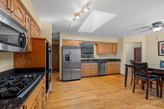 kitchen featuring a skylight, a sink, light wood finished floors, and black appliances