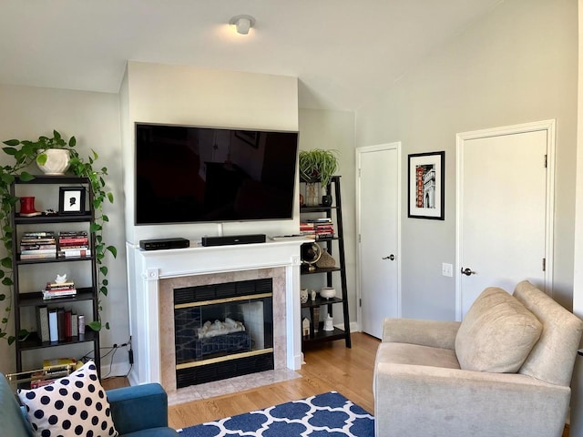 living room with a tiled fireplace, vaulted ceiling, and wood finished floors