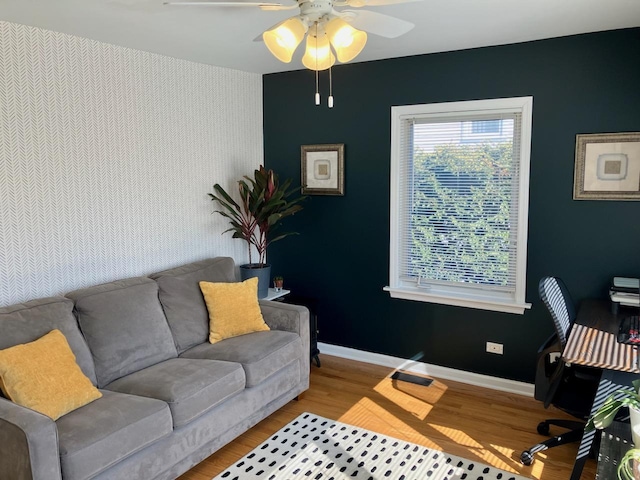 office area with an accent wall, ceiling fan, baseboards, and wood finished floors