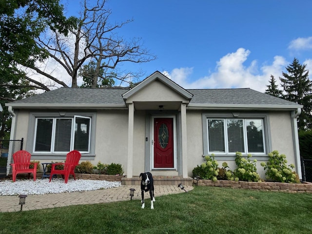 single story home featuring a shingled roof, a front lawn, and stucco siding