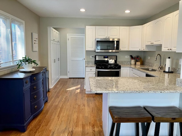 kitchen with blue cabinets, a sink, white cabinetry, a kitchen breakfast bar, and appliances with stainless steel finishes