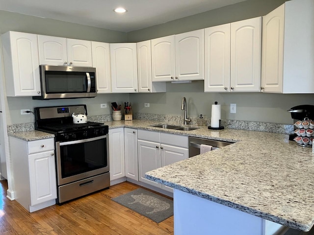 kitchen featuring appliances with stainless steel finishes, white cabinetry, a sink, and light wood finished floors