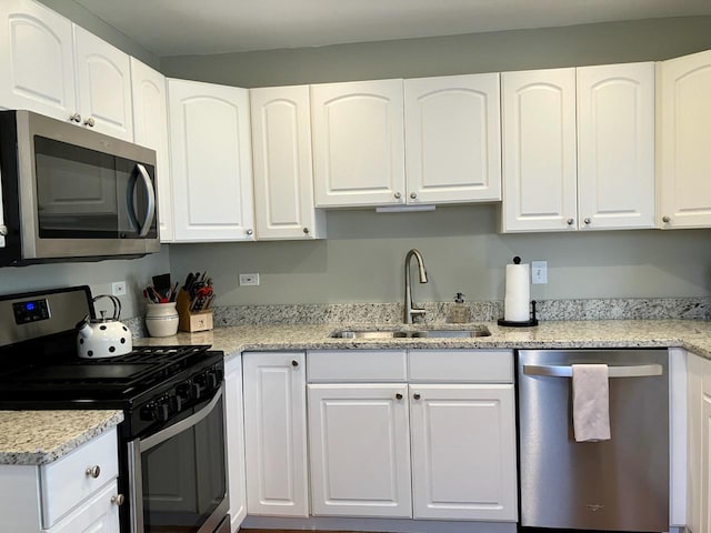 kitchen featuring light stone countertops, white cabinetry, stainless steel appliances, and a sink