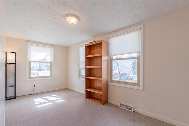 empty room with carpet floors, baseboards, visible vents, and a textured ceiling