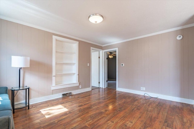 unfurnished living room with built in features, visible vents, ornamental molding, baseboards, and hardwood / wood-style flooring