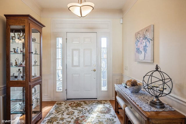 entrance foyer featuring a wainscoted wall, crown molding, a decorative wall, and wood finished floors