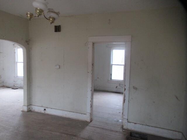 empty room featuring a wealth of natural light, arched walkways, and wood finished floors