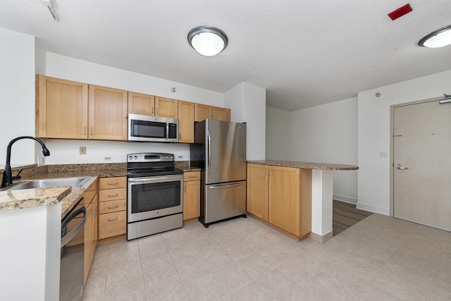 kitchen featuring a peninsula, a sink, a textured ceiling, and stainless steel appliances