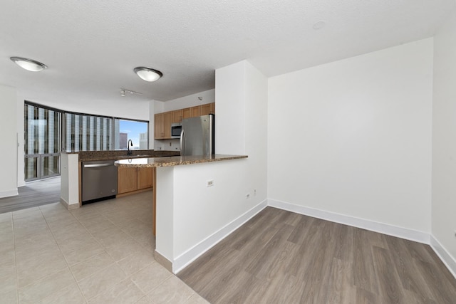 kitchen featuring a peninsula, baseboards, a textured ceiling, and stainless steel appliances
