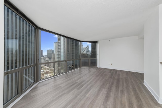 unfurnished room with a wall of windows, a city view, baseboards, and wood finished floors
