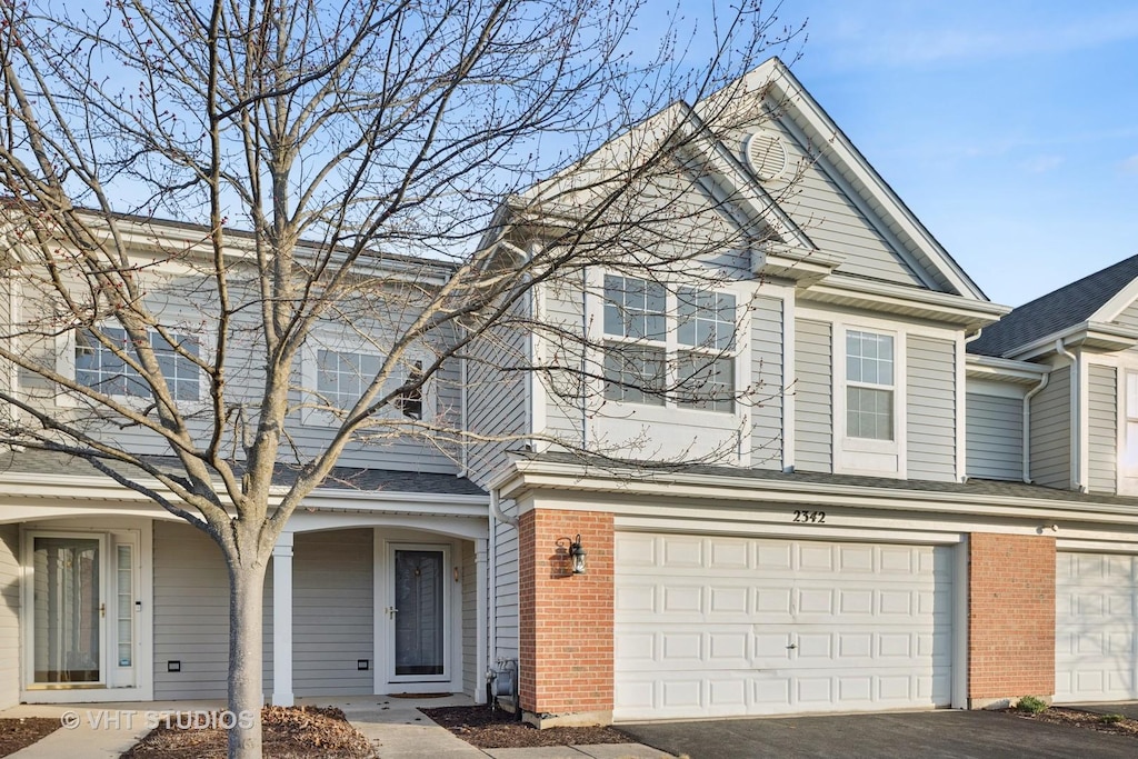 townhome / multi-family property with a garage, brick siding, and driveway