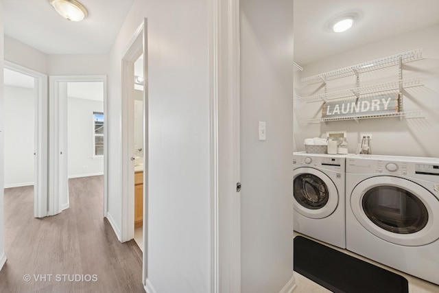 clothes washing area featuring washer and dryer, laundry area, light wood-style flooring, and baseboards