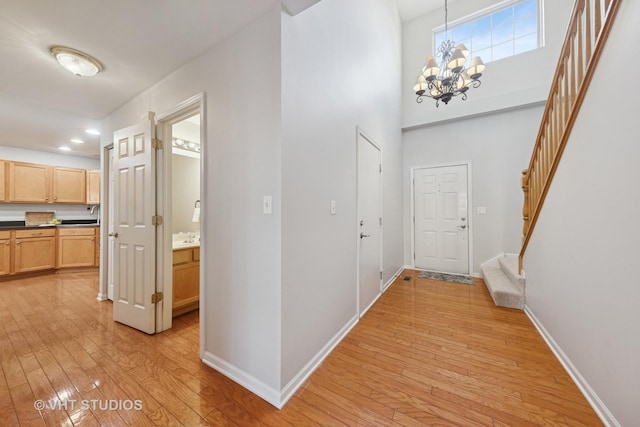 corridor featuring baseboards, stairs, light wood-style floors, and a towering ceiling