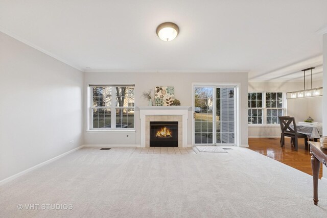 carpeted living room featuring a tiled fireplace, crown molding, visible vents, and a chandelier