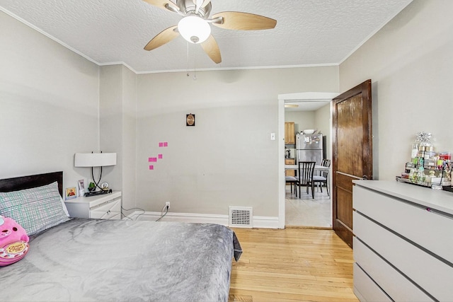 bedroom with a textured ceiling, visible vents, baseboards, ornamental molding, and light wood finished floors