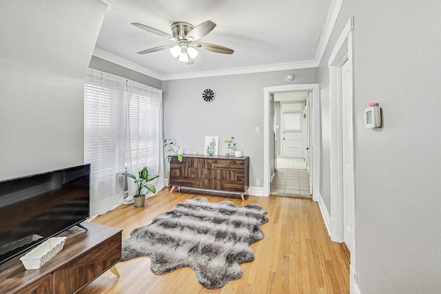 sitting room with light wood-type flooring, ceiling fan, baseboards, and crown molding