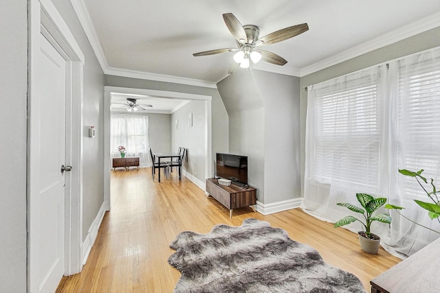 living area with crown molding, light wood-style flooring, baseboards, and ceiling fan