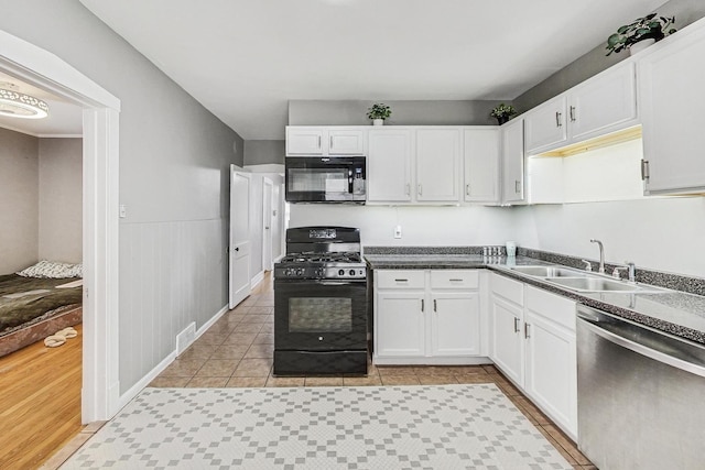 kitchen with white cabinets, wainscoting, dark countertops, black appliances, and a sink