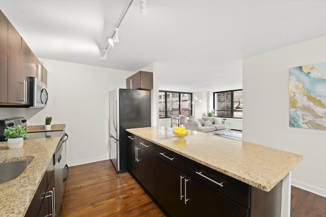 kitchen featuring dark wood finished floors, appliances with stainless steel finishes, open floor plan, light stone countertops, and a peninsula