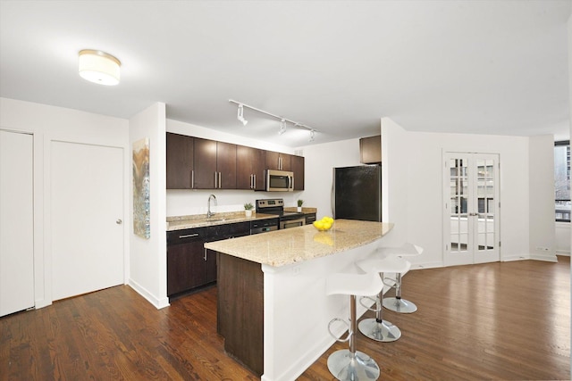 kitchen with stainless steel appliances, dark wood-type flooring, dark brown cabinets, and a kitchen bar