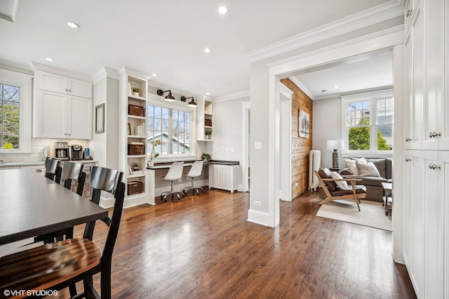 dining space with radiator, dark wood-type flooring, crown molding, built in desk, and recessed lighting