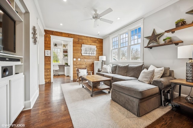 living room featuring dark wood finished floors, radiator heating unit, ornamental molding, a ceiling fan, and wood walls