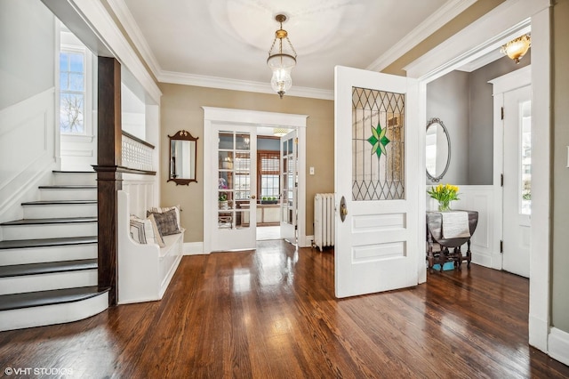 foyer featuring a wainscoted wall, wood finished floors, stairs, radiator heating unit, and crown molding