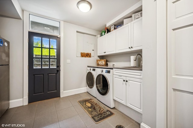 washroom featuring light tile patterned flooring, washing machine and dryer, a sink, baseboards, and cabinet space