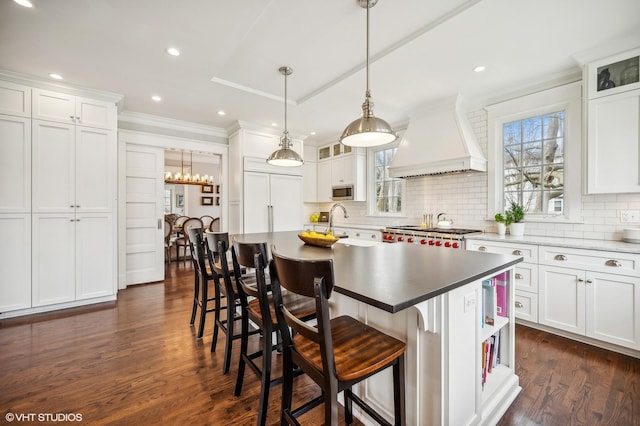 kitchen featuring range, custom range hood, stainless steel microwave, white cabinetry, and backsplash