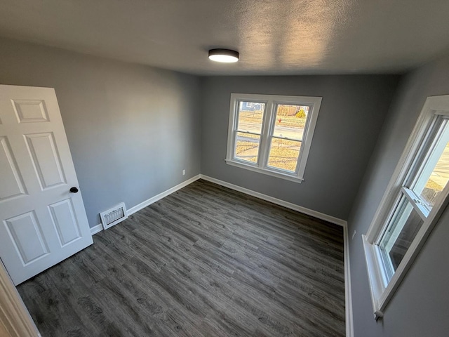 spare room featuring visible vents, dark wood finished floors, a textured ceiling, and baseboards