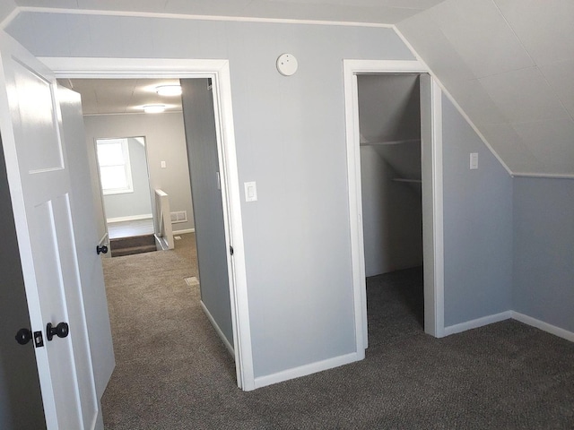 interior space featuring lofted ceiling, dark carpet, and baseboards