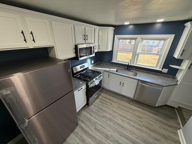 kitchen with stainless steel appliances, white cabinets, a sink, and light wood-style flooring