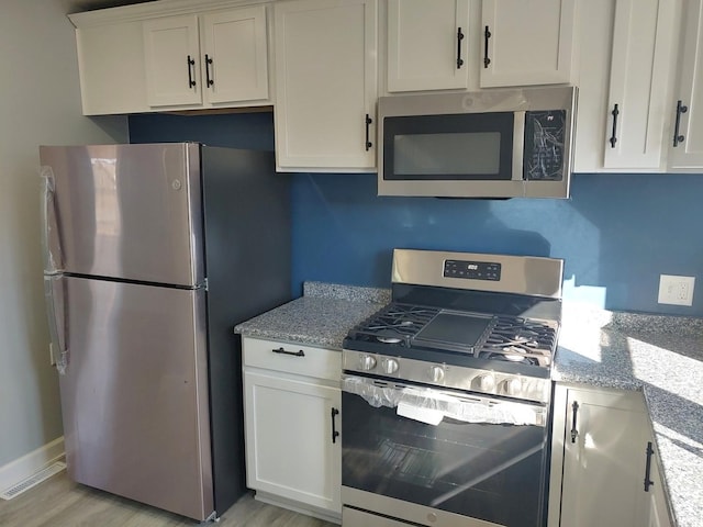 kitchen with light stone counters, light wood-style flooring, stainless steel appliances, visible vents, and white cabinetry