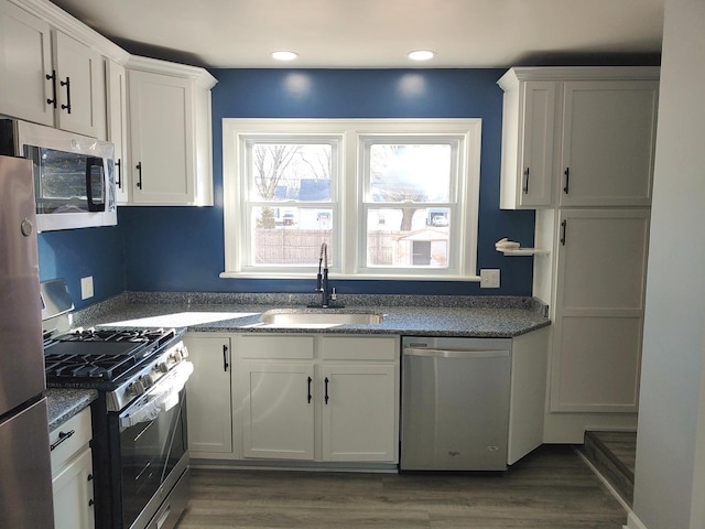 kitchen with wood finished floors, appliances with stainless steel finishes, a sink, and white cabinetry