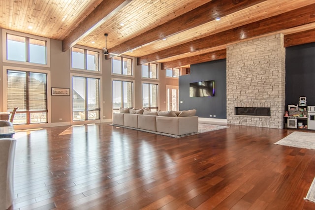 unfurnished living room featuring beam ceiling, wood finished floors, a stone fireplace, baseboards, and a towering ceiling