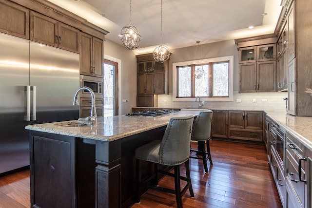 kitchen featuring backsplash, dark wood-type flooring, built in appliances, an inviting chandelier, and a sink