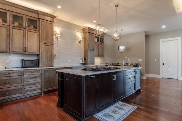 kitchen featuring gas cooktop, dark wood-style floors, a center island with sink, and backsplash