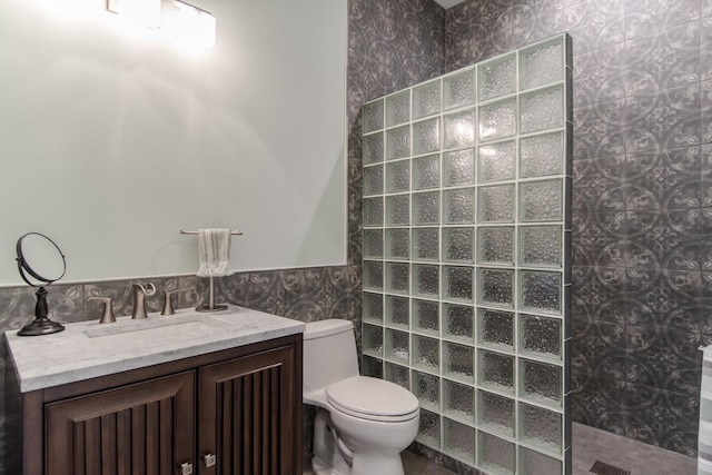 bathroom with a wainscoted wall, toilet, tile walls, walk in shower, and vanity