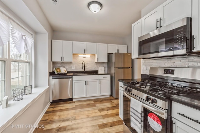 kitchen with stainless steel appliances, light wood-style floors, white cabinets, and a sink