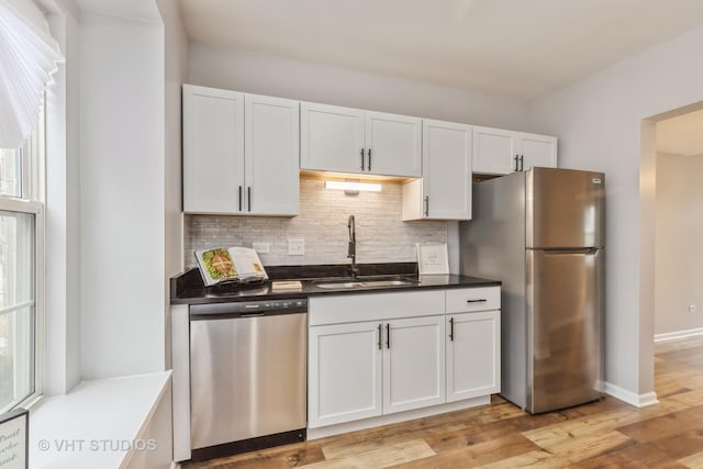 kitchen featuring white cabinets, light wood-style flooring, a sink, stainless steel appliances, and backsplash