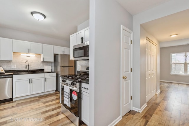 kitchen featuring dark countertops, decorative backsplash, appliances with stainless steel finishes, white cabinets, and a sink