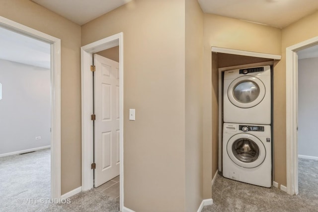 laundry area featuring carpet, laundry area, baseboards, and stacked washing maching and dryer