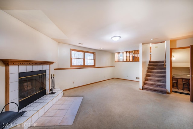 unfurnished living room with carpet floors, stairway, baseboards, and a tiled fireplace