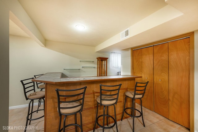 bar with light tile patterned floors, bar area, visible vents, and baseboards