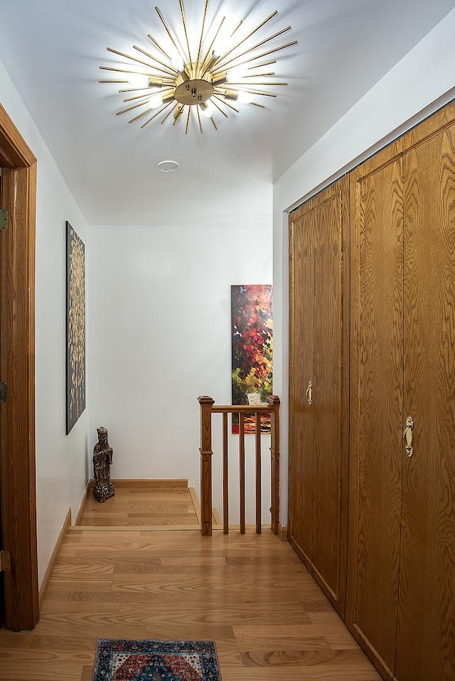 hall featuring baseboards, light wood-style flooring, an upstairs landing, and an inviting chandelier