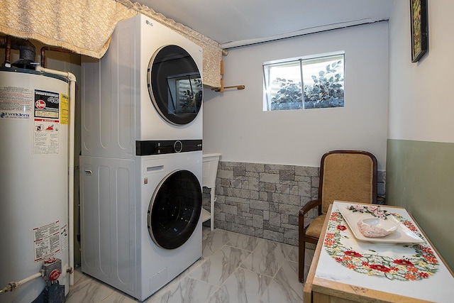 laundry room featuring laundry area, water heater, marble finish floor, and stacked washer / dryer