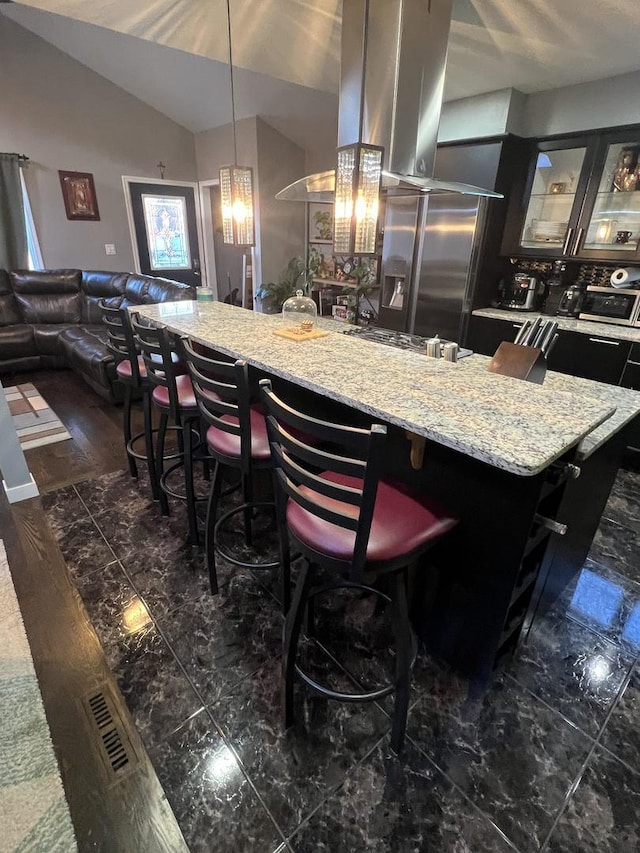 kitchen with light stone counters, a breakfast bar area, glass insert cabinets, vaulted ceiling, and stainless steel fridge