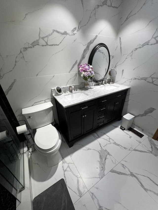 bathroom with stone wall, double vanity, a sink, and toilet